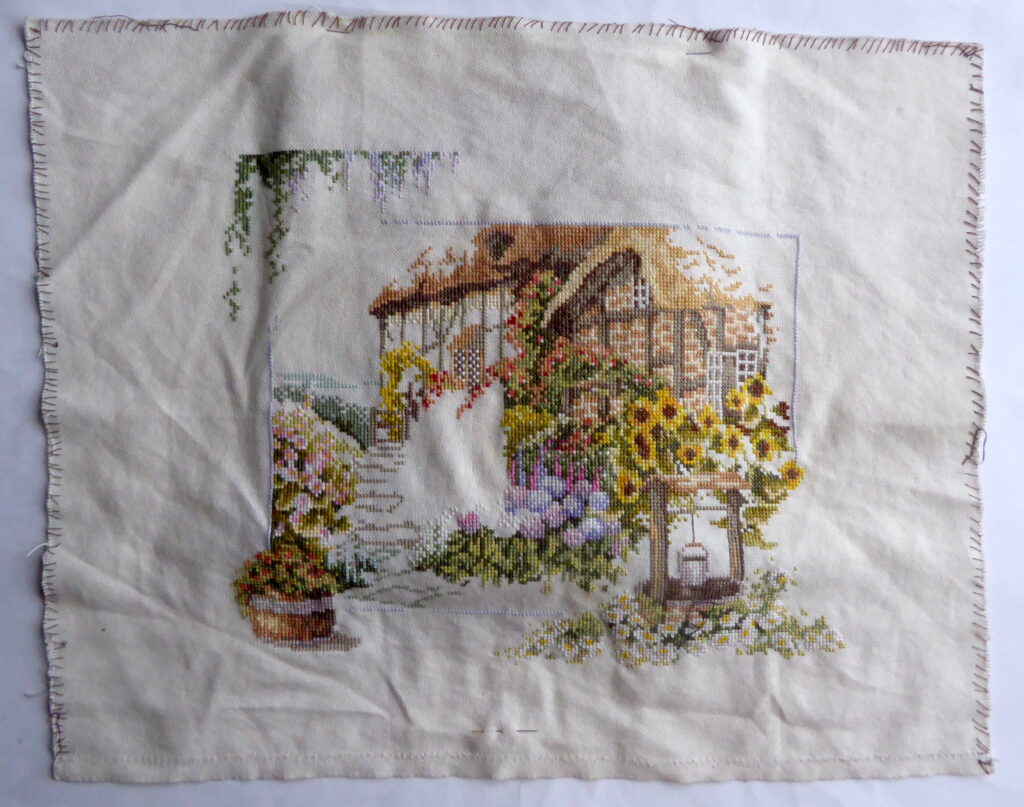 Onaf in kruissteek geborduurde cottage met waterput en bloemen